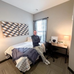 a person smiling leaning on a bed in a bedroom